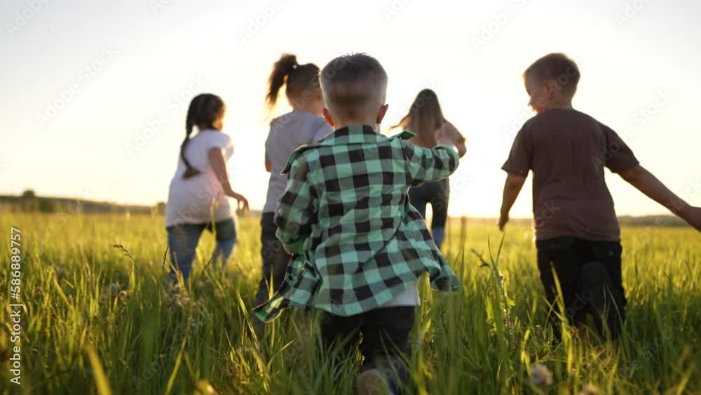 Group of happy children run walk on grass park. Cheerful smile of cute children in nature in meadow. Team of children are playing in green grass. Active movement and joy of children at sunset in field