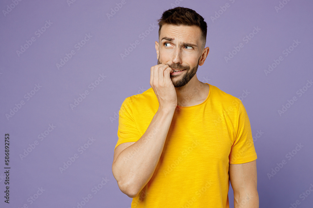 Young sad mistaken confused embarrassed caucasian man wear yellow t-shirt look aside on area biting nails fingers isolated on plain pastel light purple background studio portrait. Lifestyle concept. Young sad mistaken confused embarrassed caucasian man wear yellow t-shirt look aside on area biting nails fingers isolated on plain pastel light purple background studio portrait. Lifestyle concept.