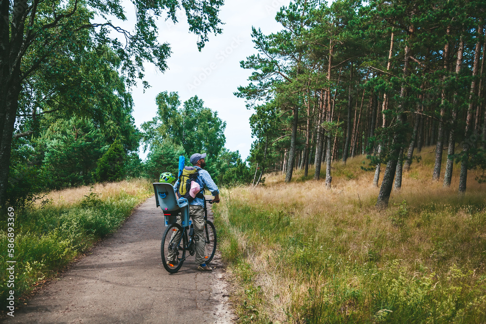 Naklejka premium Father and his little child travelling by bike in the forest, the girl is sitting in the child seat