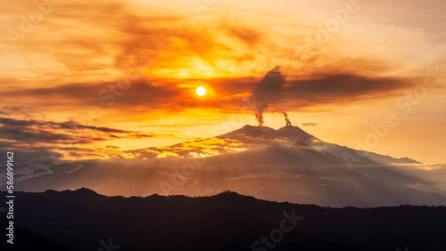 Fotografia mysterious landscape of great erupting volcano with smoke from craters and snow on slopes in orange light of sunset