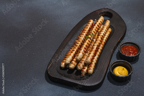 Roasted pork meat sausages on wooden board. Set of sauces  traditional food for picnic or BBQ