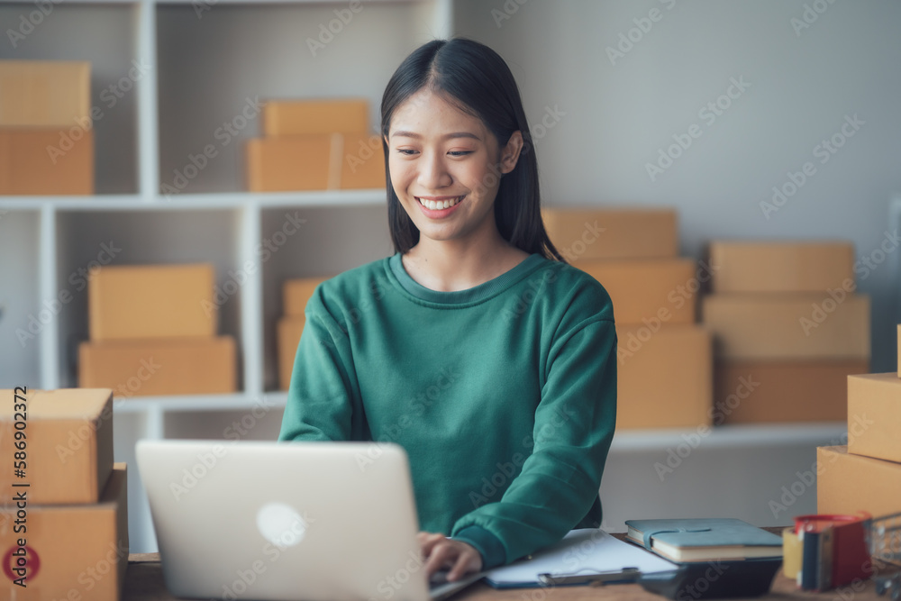 Startup small business entrepreneur or freelance Asian woman using a laptop with box, Young success Asian woman with her hand lift up, online marketing packaging box and delivery, SME concept. Startup small business entrepreneur or freelance Asian woman using a laptop with box, Young success Asian woman with her hand lift up, online marketing packaging box and delivery, SME concept.