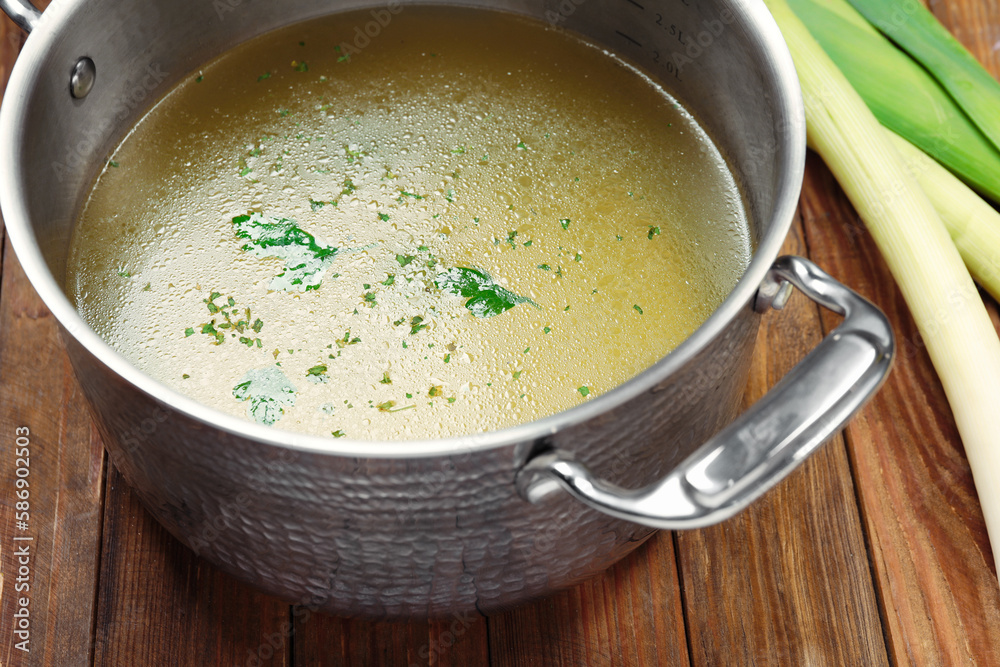 Pot with tasty bouillon and celery on wooden table, closeup Pot with tasty bouillon and celery on wooden table, closeup