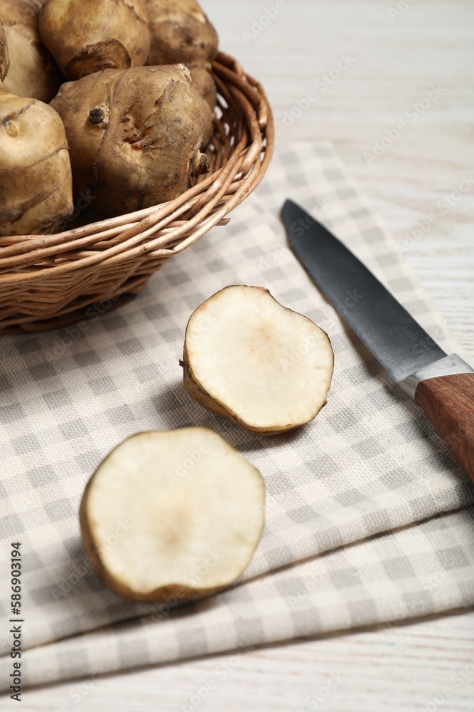 Fototapeta premium Wicker basket and many Jerusalem artichokes with knife on white wooden table