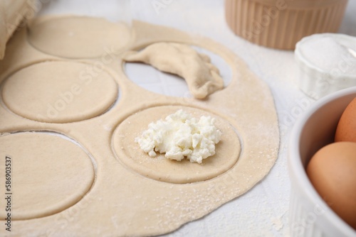Process of making dumplings (varenyky) with cottage cheese. Raw dough and other ingredients on white tiled table, closeup