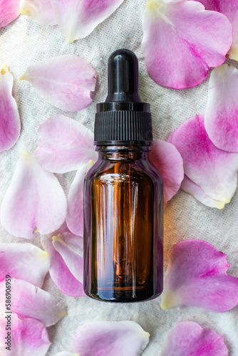 Glass dropper bottle and rose petals on canvas background. The concept of natural cosmetics. Vertical image.