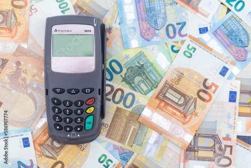 Pos payment terminal and Euro banknotes of different denominations on background.