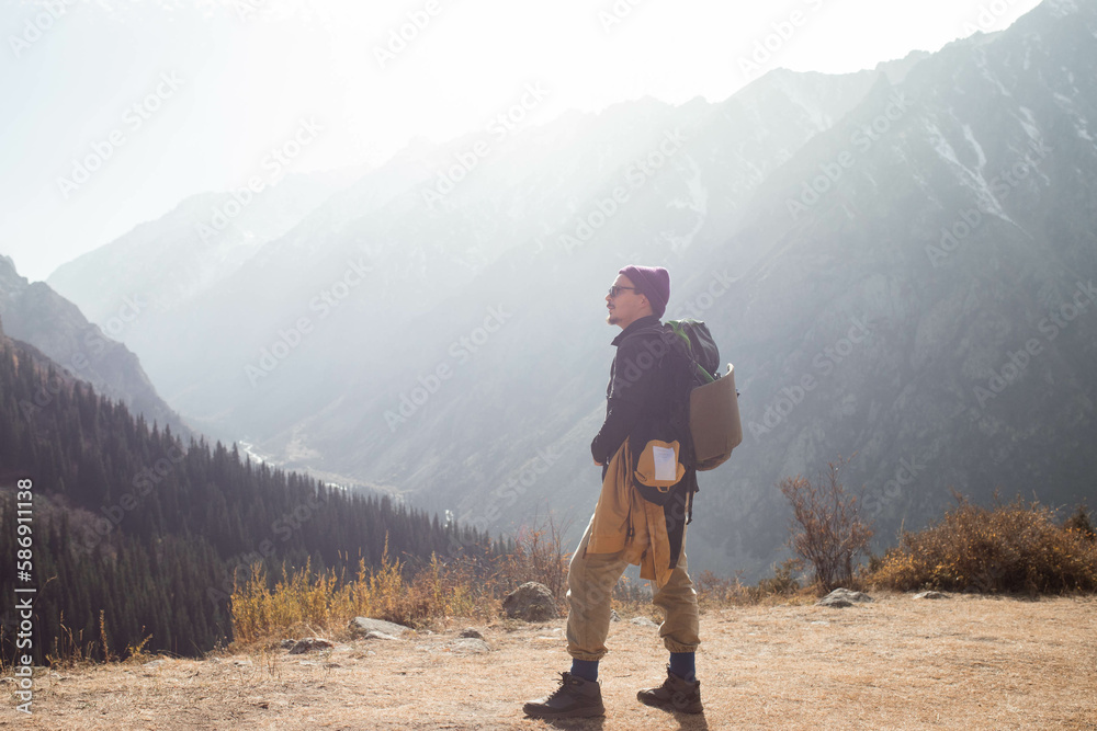 In the photo, a man is captured from behind, standing with a broad view of the mountains ahead. His gaze is fixed on the scenic mountainscape