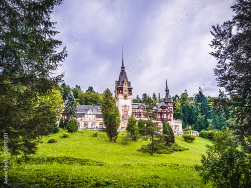 Front View Of The Peles Castle With Trees And Bushes In The Foreground