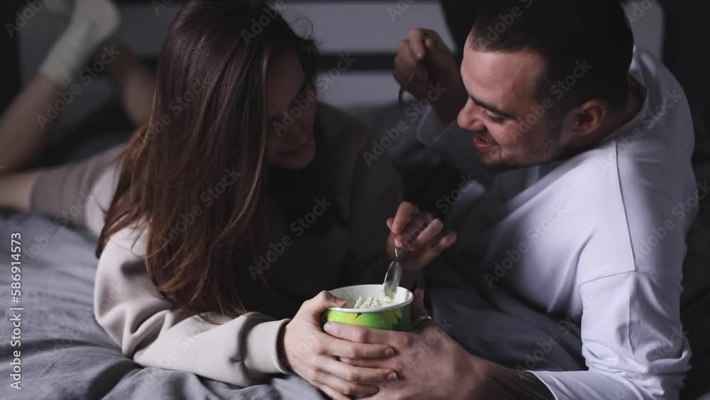 Cheerful couple eating pistachio ice cream lying in the bed at home and talking. Dating. Couple have fun at home. Love relationship concept. Cheerful couple eating pistachio ice cream lying in the bed at home and talking. Dating. Couple have fun at home. Love relationship concept.