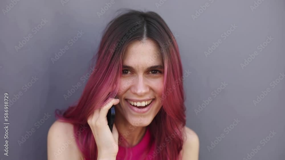 Pink hair woman talking on mobile phone covering mouth with hands, make shh gesture, hold finger near mouth. Can not speak over isolated grey background. Pink hair woman talking on mobile phone covering mouth with hands, make shh gesture, hold finger near mouth. Can not speak over isolated grey background.