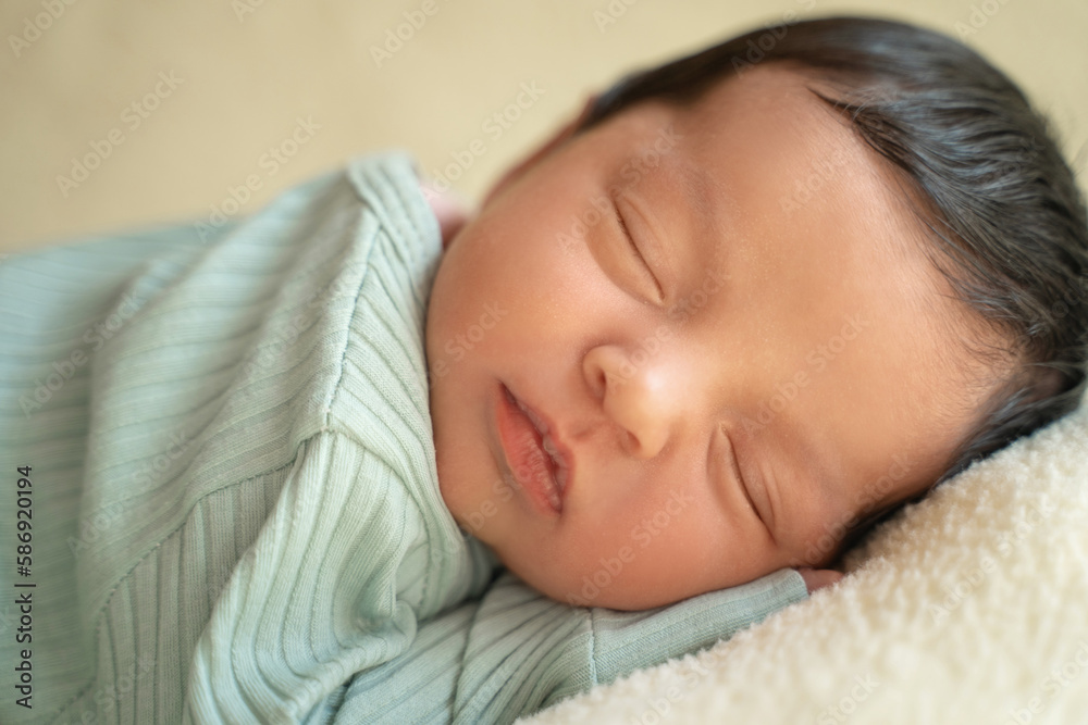Newborn baby infant with dark hair lying on side sleeping awaking open eyes. Cute little Middle eastern child on blanket. Tranquil scene close up
