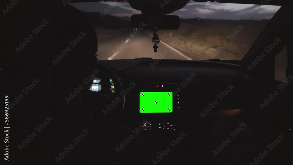 Man driving modern sports car on a highway in evening time using navigation on his smart phone with blank green screen