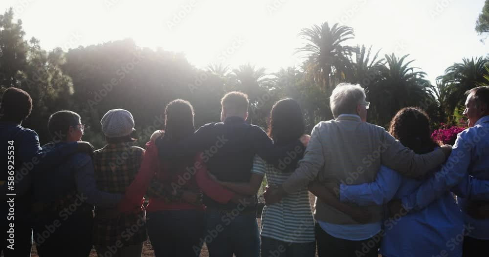 Crowd of multigenerational people hugging each other in front of camera - Multiracial friends with different ages having fun together at city park 