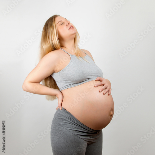 Free Download A pregnant girl, on a gray background. Big stomach, back pain. - GFXLoad