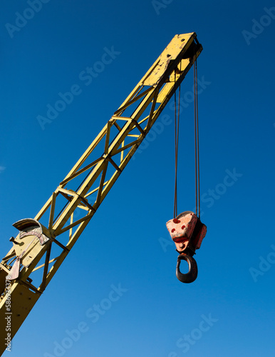 Old yellow battered crane-boom and hook against the blue sky.