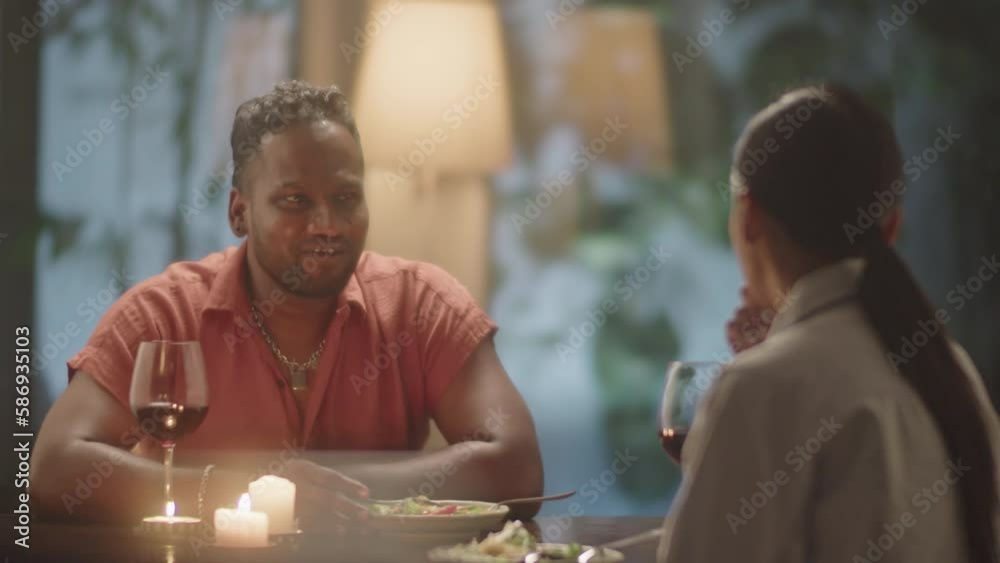 Cheerful couple smiling and chatting over dinner while having romantic date in evening at home Cheerful couple smiling and chatting over dinner while having romantic date in evening at home