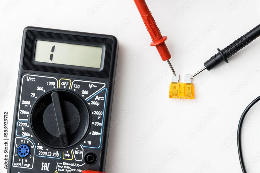 Checking faulty colored automotive fuse with digital multimeter on white background Checking faulty colored automotive fuse with digital multimeter on white background