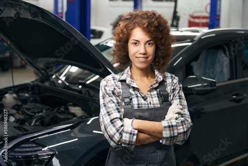 Charming employee of a car repair shop stands by car