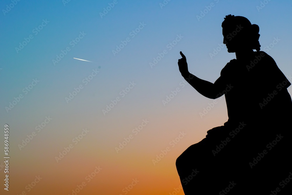 silhouette of a statue pointing to an airplane at sunset