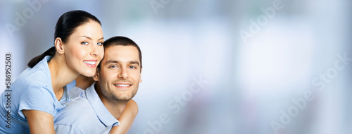 Happy amazed smiling couple. Portrait of standing close embracing models in love concept, indoors. Young brunette man and woman. Wide image.