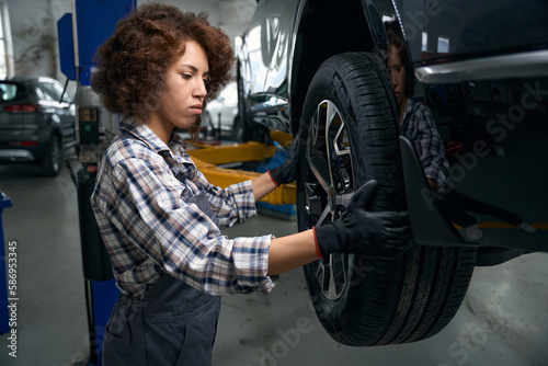 Woman auto mechanic carefully examines a car wheel