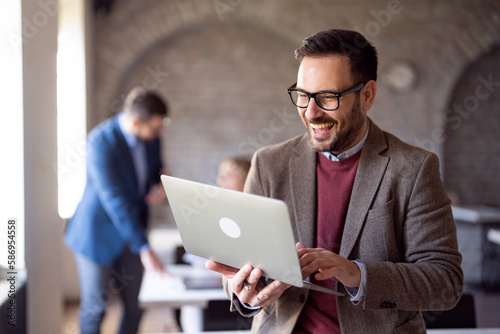 Smart entrepreneur holding laptop and smiling at office