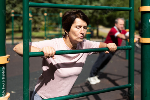 Aged woman doing exercises on sports bars in open-air sports area