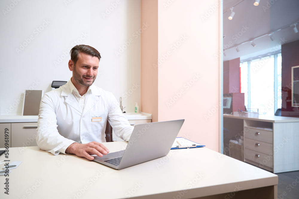 Positive doctor is looking to the screen of computer in ophthalmology center Positive doctor is looking to the screen of computer in ophthalmology center