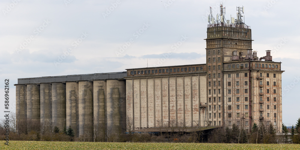 A huge concrete grain silo standing in a field. Warehouses full of grain before the new season