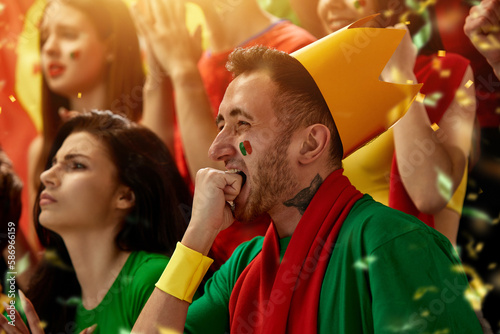Portugal football fans emotionally watching match, game at stadium, supporting and cheering up team during tense moment. Concept of sport, competition, championship, emotions, hobby and entertainment