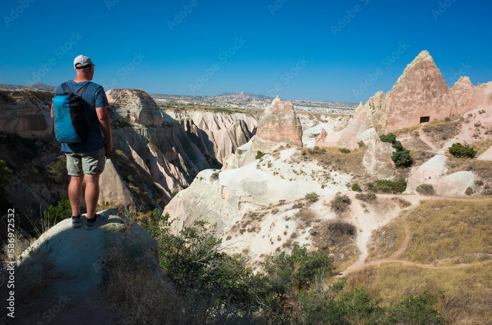 Tourist in Cappadocia, Anatolia region, travel Turkey. Man stands on hill with view of Red Valley landscape, weathered ancient volcanic ash canyon