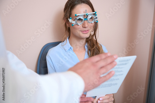 Happy smiling female in trial frame is examining her eyesight in the hospital