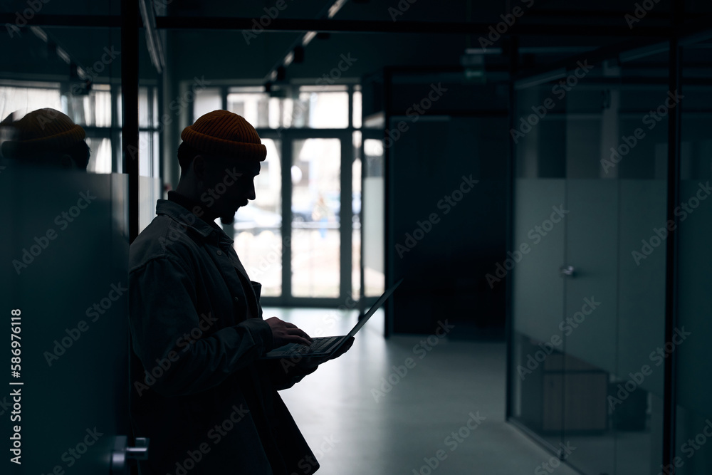 Focused office worker working on laptop in dark corridor Focused office worker working on laptop in dark corridor