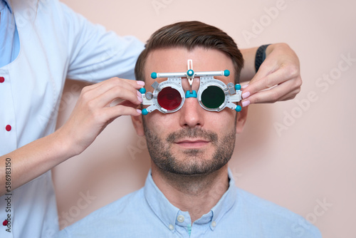 Confident bearded man examining g his eyesight with trial frame in the hospital