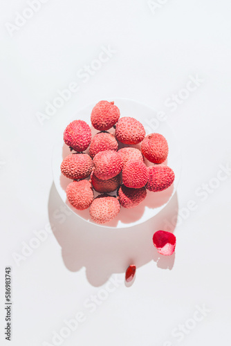 Fototapeta Naklejka Na Ścianę i Meble -  Minimal style composition made of fresh lychee fruits on a plate on white background with  shadow. Summer refreshment concept. Still life. Top view. Flat lay