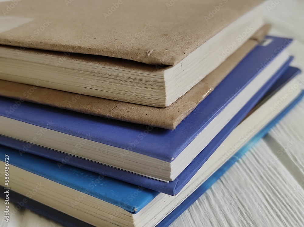 Three books in a stack with closed pages on a white wooden background