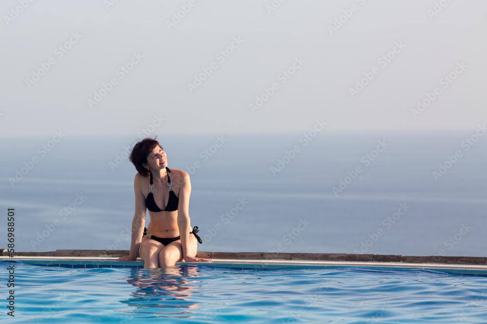Woman sunbathing near the pool in a luxury hotel overlooking the ocean. Woman sunbathing near the pool in a luxury hotel overlooking the ocean.