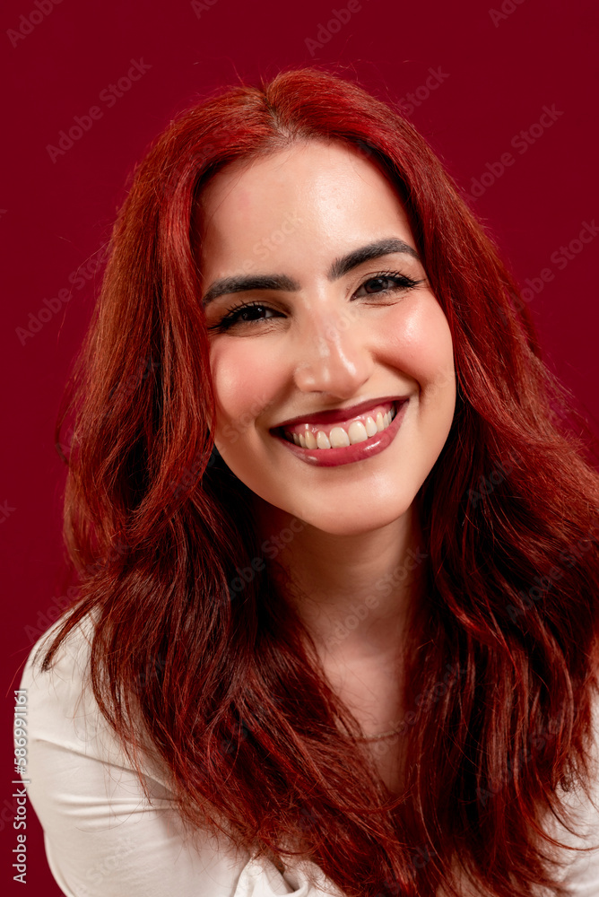Confident woman looking at the camera and smiling while posing against a red isolated background. Confident woman looking at the camera and smiling while posing against a red isolated background.