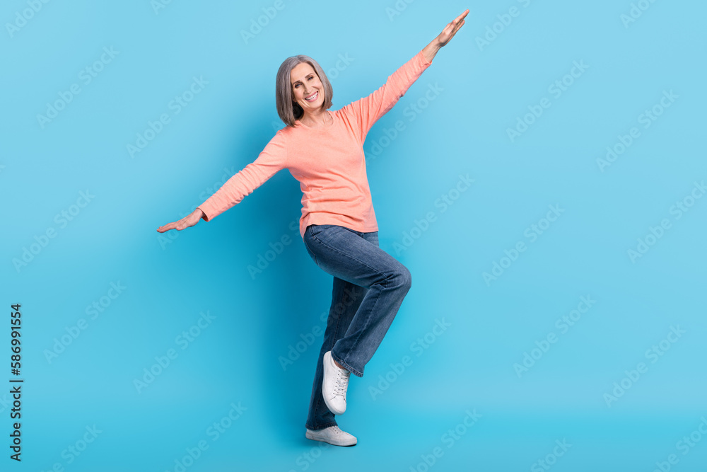 Full length photo of carefree feel young retired lady hands wings have fun flying satisfied wear trendy clothes isolated on blue color background