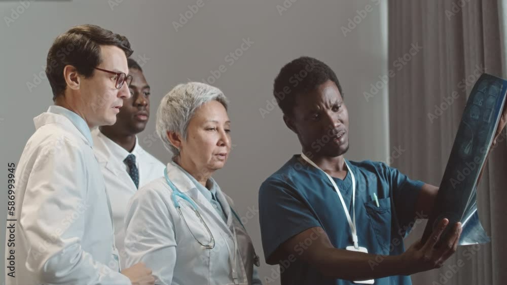 Multiethnic doctors team looking at MRI of human brain and talking standing by window in medical office Multiethnic doctors team looking at MRI of human brain and talking standing by window in medical office