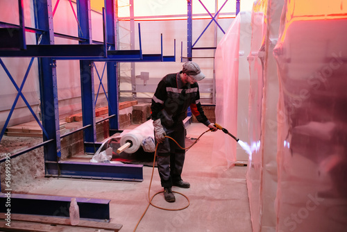 Foto Factory worker packing goods by film using blowtorch