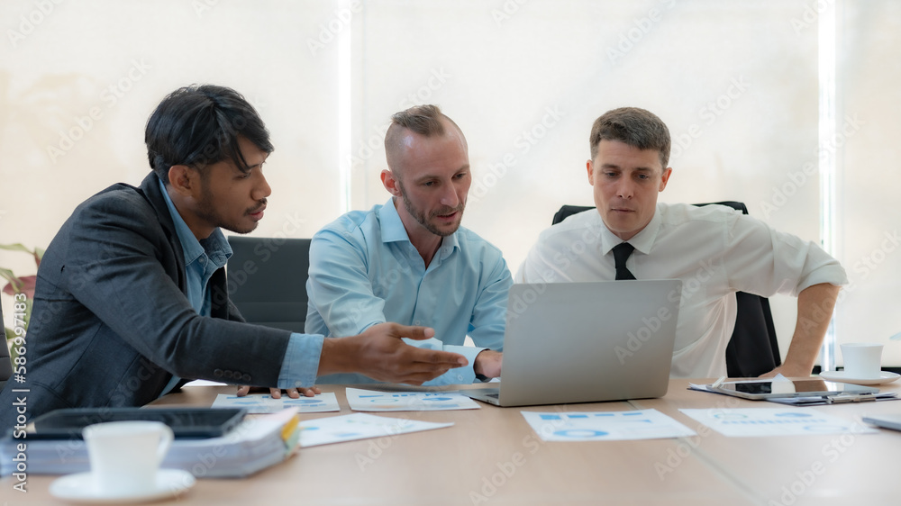 Group of diverse businessman going over paperwork together and working on laptop at meeting.