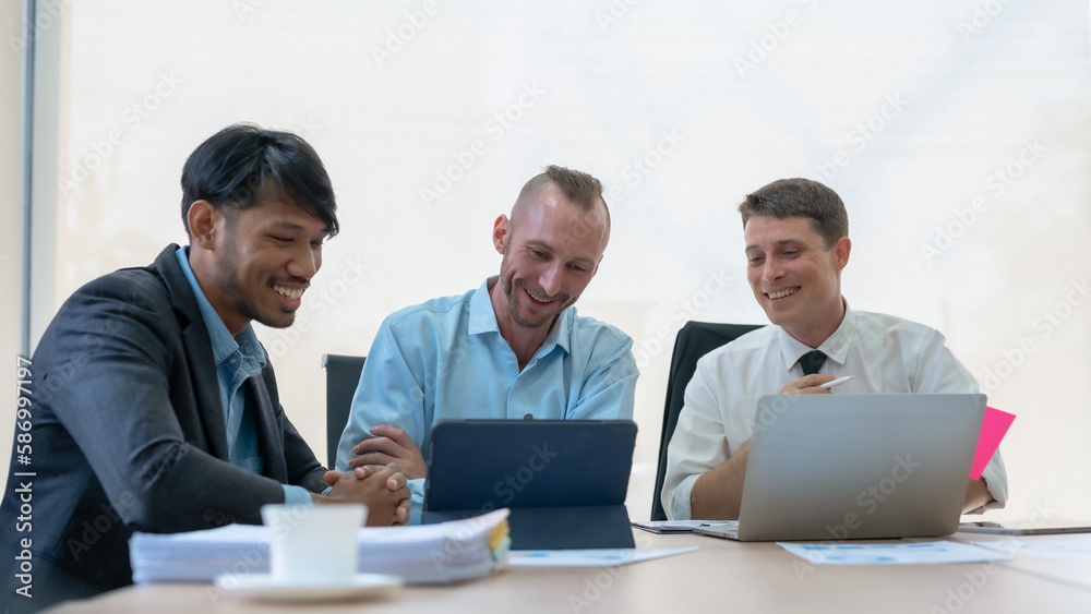 Group of diverse businessman going over paperwork together and working on laptop at meeting.