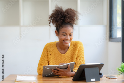Woman student using tablet and holding book preparing for online class.
