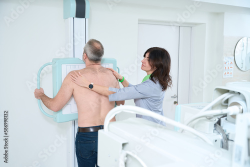 Adult man standing in a medical gown undergoing a chest x-ray procedure