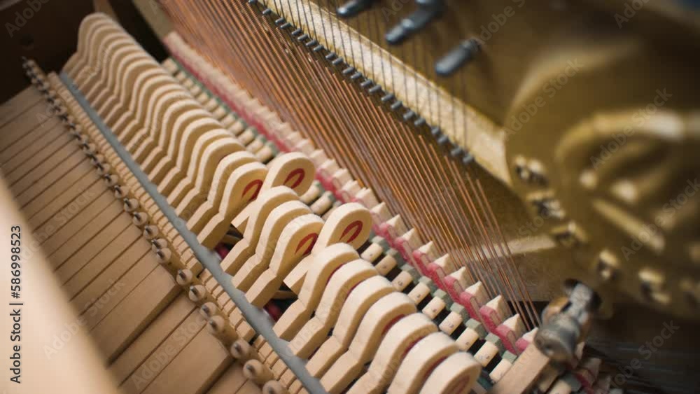 Several piano hammers strike piano strings in an old home piano upright piano made of light wood.