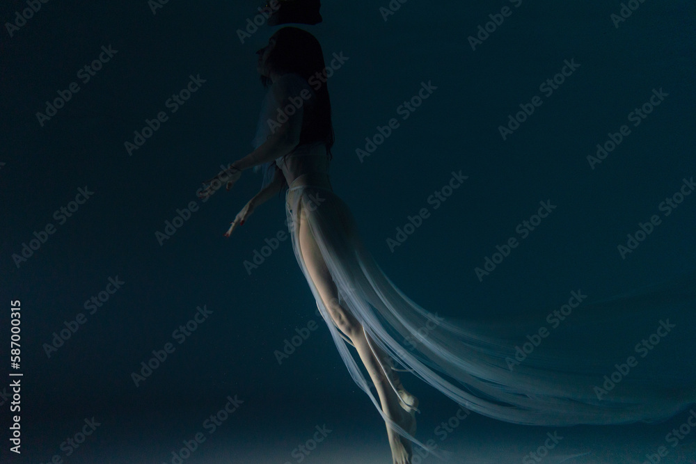 Obraz premium Underwater shoot of beautiful woman in white flying transparent dress swimming in water through sunbeams.