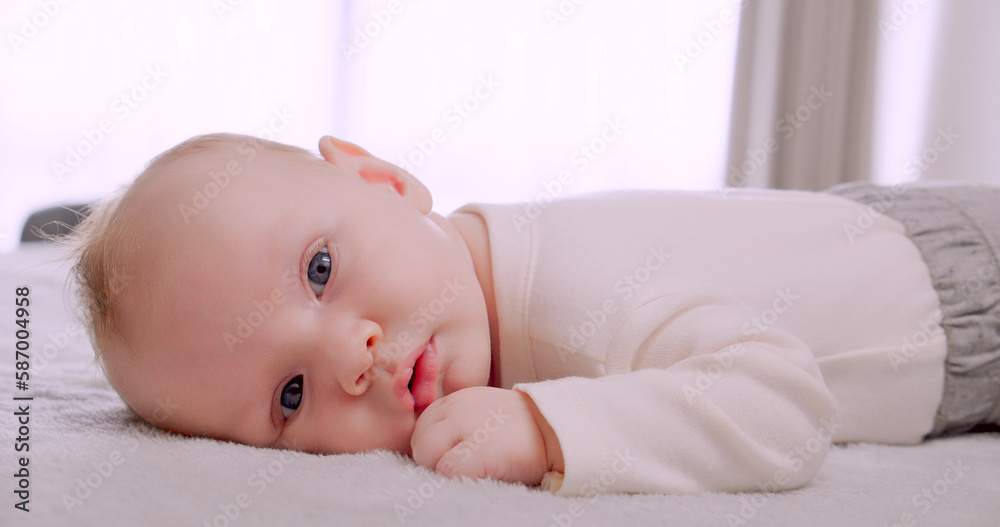 Portrait of a newborn baby looking at the camera. One-month-old baby is lying on his tummy in light clothes. White calm little boy looks at the camera. Close-up of a cute boy's face. Children concept.