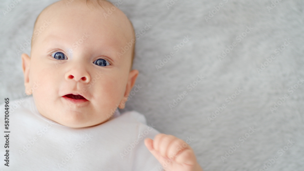 Child's face of a Happy newborn baby looking to camera. Healthy newborn baby in a white t-shirt with blue eyes. Face of a Beautiful active tiny child. Cute white Infant boy, top view. Child's face of a Happy newborn baby looking to camera. Healthy newborn baby in a white t-shirt with blue eyes. Face of a Beautiful active tiny child. Cute white Infant boy, top view.